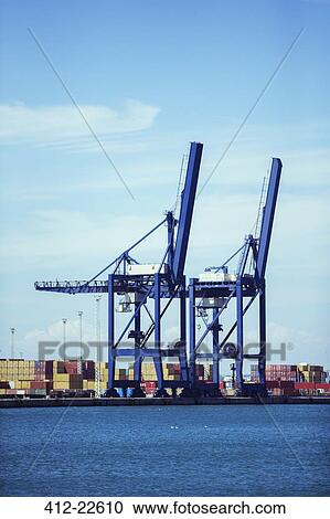 Stock Image - Cranes and cargo containers at waterfront. Fotosearch