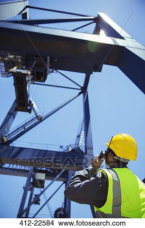 Picture - Low angle view of worker using walkie-talkie near crane. Fotosearch