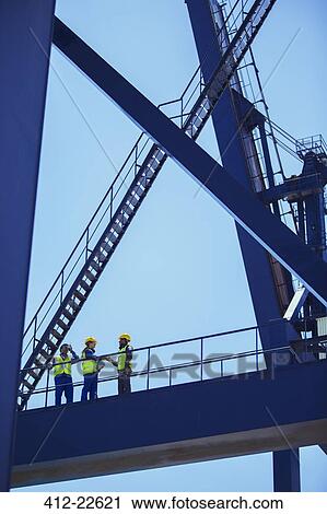 Low angle view of workers and businessman talking on cargo crane View Large Photo Image Stock Image - Low angle view of workers and businessman talking on cargo crane. Fotosearch