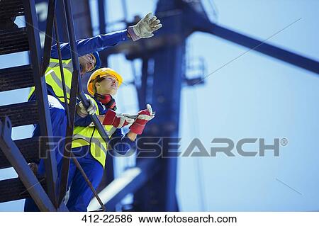 Stock Photograph - Low angle view of workers talking on crane. Fotosearch
