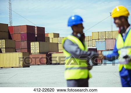 Stock Image - Worker and businessman shaking hands near cargo containers. Fotosearch