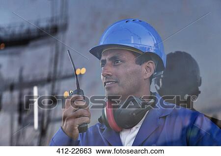 Stock Image - Worker holding walkie-talkie near window. Fotosearch