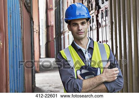Stock Image - Worker standing between cargo containers. Fotosearch