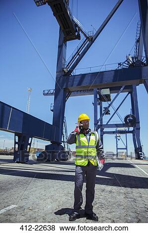 Worker talking on cell phone near cargo crane View Large Photo Image Stock Photo - Worker talking on cell phone near cargo crane. Fotosearch