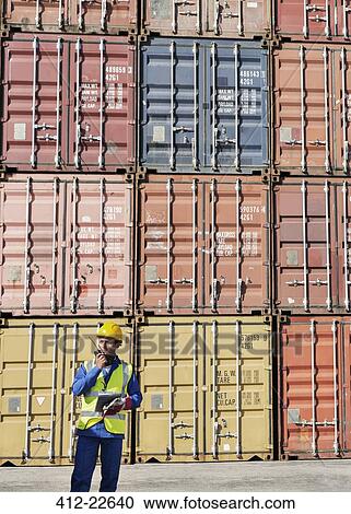 Stock Image - Worker using walkie-talkie near cargo containers. Fotosearch