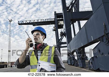 Stock Photo - Worker using walkie-talkie near crane. Fotosearch