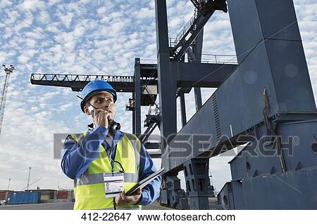 Worker using walkie-talkie under cargo crane View Large Photo Image Stock Photo - Worker using walkie-talkie under cargo crane. Fotosearch