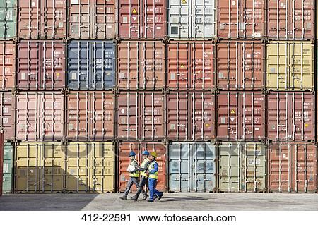 Stock Image - Workers walking together near stack of cargo containers. Fotosearch