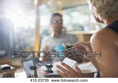Stock Photography - Business people eating sushi in office. Fotosearch