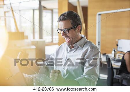 Stock Photograph - Businessman cheering at office desk. Fotosearch