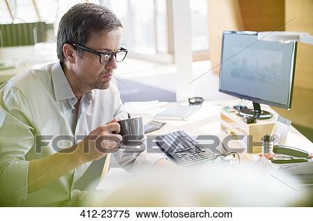 Businessman drinking cup of coffee at office desk View Large Photo Image Stock Photography - Businessman drinking cup of coffee at office desk. Fotosearch