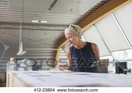Picture - Businesswoman reading paperwork in office. Fotosearch