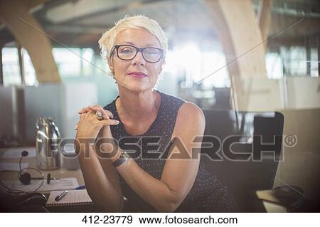 Businesswoman sitting with hands clasped at office desk View Large Photo Image Stock Photo - Businesswoman sitting with hands clasped at office desk. Fotosearch