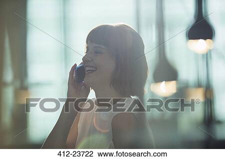 Stock Image - Businesswoman talking on cell phone in office. Fotosearch