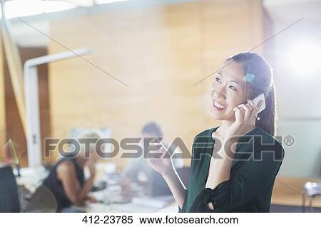 Stock Photography - Businesswoman talking on cell phone in office. Fotosearch