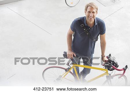Stock Image - Smiling man standing with bicycle. Fotosearch
