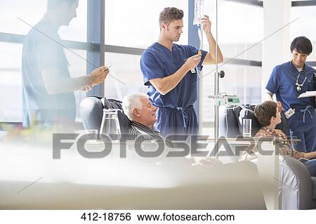 Stock Photograph - Doctors attending patients receiving intravenous infusion in hospital. Fotosearch
