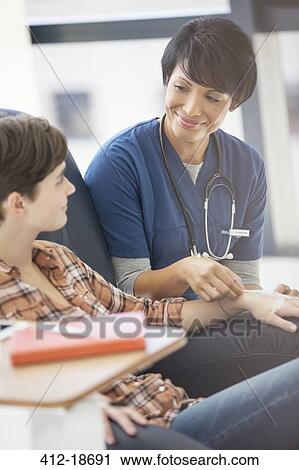 Stock Image - Female doctor talking to young patient receiving medical treatment in hospital ward. Fotosearch
