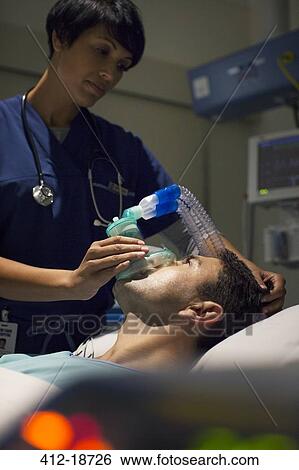 Stock Photograph - Female doctor wearing mask anesthetizing mid adult man in hospital ward. Fotosearch