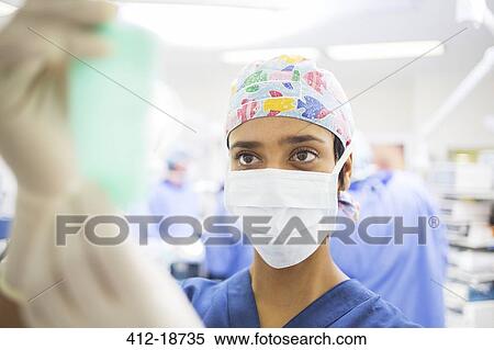 Stock Photography - Masked surgeon adjusting saline bag during surgery. Fotosearch