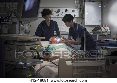 Stock Image - Mature female doctor and female nurse examining patient's throat. Fotosearch