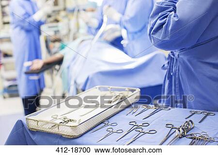 Stock Image - Nurse standing by tray with surgical tools in operating theater. Fotosearch