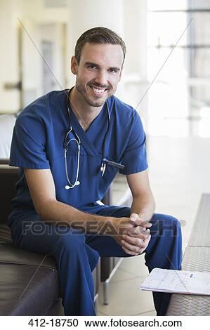 Stock Image - Portrait of male doctor sitting on sofa in hospital. Fotosearch