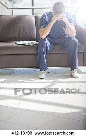 Portrait of young doctor with head in hands sitting on sofa View Large Photo Image Stock Photo - Portrait of young doctor with head in hands sitting on sofa. Fotosearch