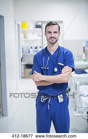 Stock Photo - Portrait of young male doctor standing in hospital ward with arms crossed. Fotosearch