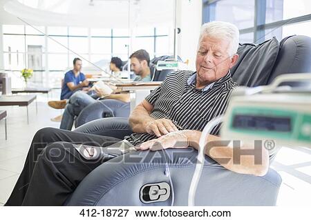 Senior patient receiving medical treatment sitting and looking down in hospital ward View Large Photo Image Stock Photo - Senior patient receiving medical treatment sitting and looking down in hospital ward. Fotosearch
