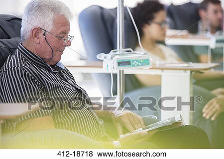 Stock Photo - Senior patient receiving treatment while sitting and reading book in hospital ward. Fotosearch