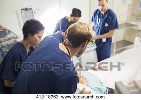 Stock Image - Team of doctors attending patient in hospital. Fotosearch
