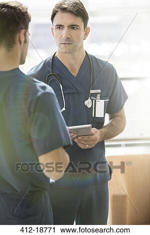 Two male doctors talking, one holding tablet pc View Large Photo Image Stock Image - Two male doctors talking, one holding tablet pc. Fotosearch