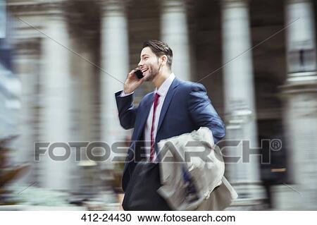 Stock Image - Blurred view of businessman talking on cell phone in city. Fotosearch