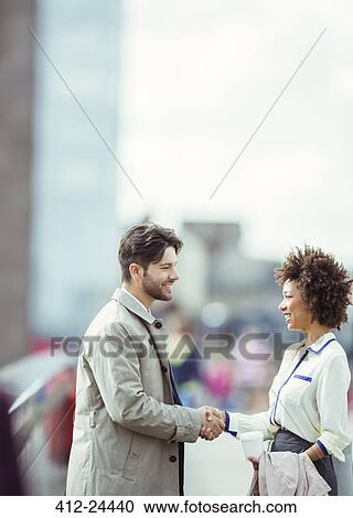 Stock Image - Business people shaking hands outdoors. Fotosearch