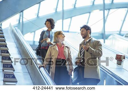 Stock Image - Business people talking on escalator. Fotosearch
