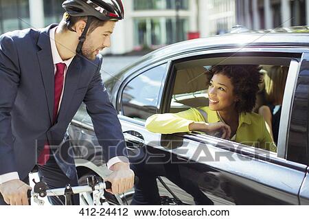 Stock Image - Businessman on bicycle talking to woman in car. Fotosearch