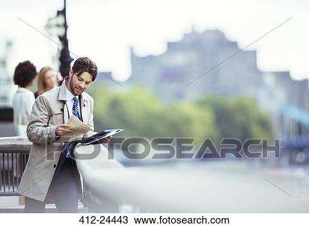 Stock Image - Businessman reading newspaper on urban waterfront. Fotosearch
