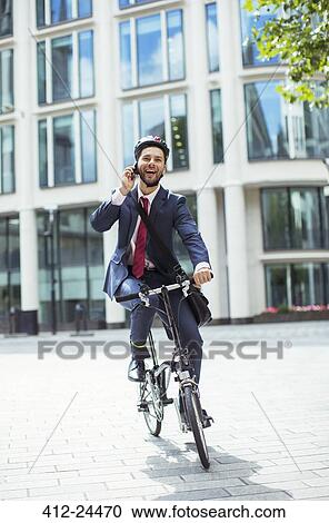 Stock Image - Businessman talking on cell phone on bicycle. Fotosearch