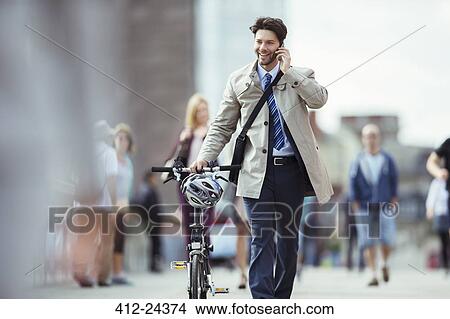 Businessman talking on cell phone pushing bicycle in city View Large Photo Image Picture - Businessman talking on cell phone pushing bicycle in city. Fotosearch
