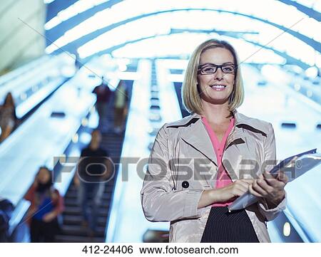 Stock Photograph - Businesswoman carrying folders near escalator. Fotosearch