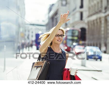 Stock Image - Businesswoman hailing taxi in city. Fotosearch