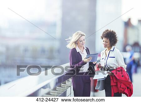 Stock Photo - Businesswomen using digital tablet on urban bridge. Fotosearch