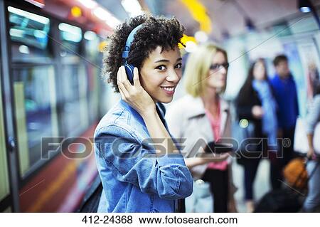Smiling woman listening to headphones in subway View Large Photo Image Stock Photo - Smiling woman listening to headphones in subway. Fotosearch