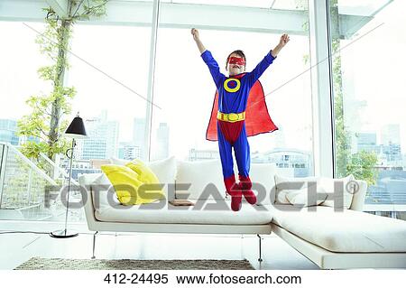 Stock Photography - Boy superhero jumping off living room sofa. Fotosearch