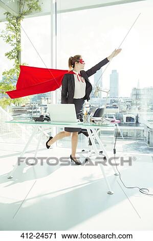 Businesswoman preparing to fly in cape and mask in office View Large Photo Image Stock Image - Businesswoman preparing to fly in cape and mask in office. Fotosearch