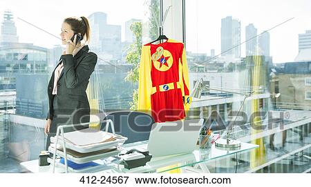 Businesswoman talking on cell phone with superhero costume behind her View Large Photo Image Stock Photo - Businesswoman talking on cell phone with superhero costume behind her. Fotosearch