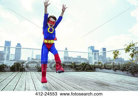 Stock Image - Superhero boy jumping on city rooftop. Fotosearch