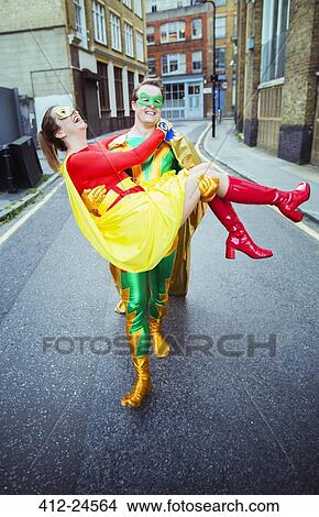 Picture - Superhero carrying wife on city street. Fotosearch