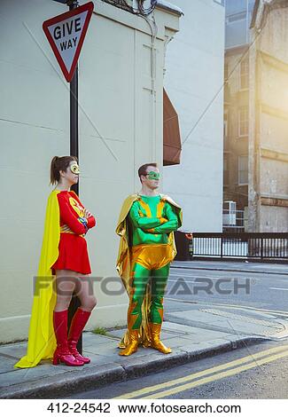 Stock Image - Superhero couple waiting at corner on city sidewalk. Fotosearch